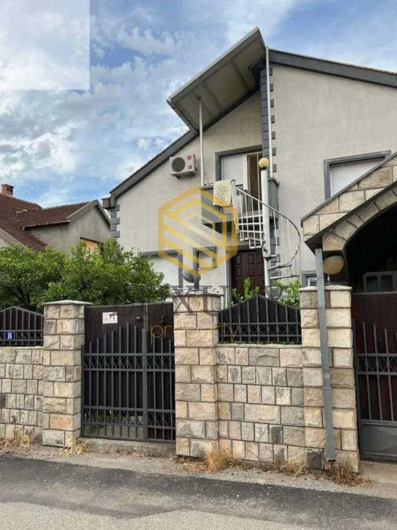 Eksterijer kuće sa dvorišnom ogradom i spiralnim stepeništem.