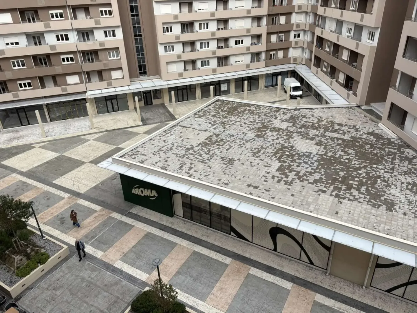 Pogled sa visine na popločano dvorište i fasadu modernog stambeno-poslovnog kompleksa.