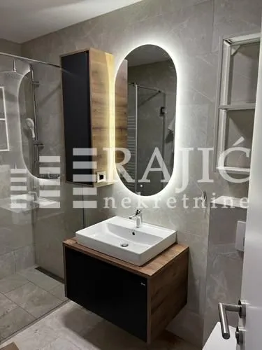 Modern bathroom with a washbasin, backlit mirror, and shower enclosure.