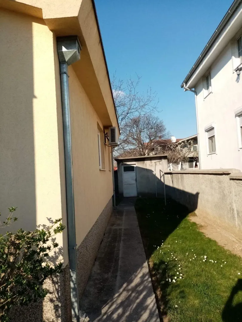 A narrow paved pathway beside the house with a small lawn and an auxiliary building.