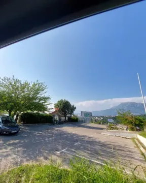 Asphalted parking space in front of the building with a view of surrounding greenery and mountains. - image 9