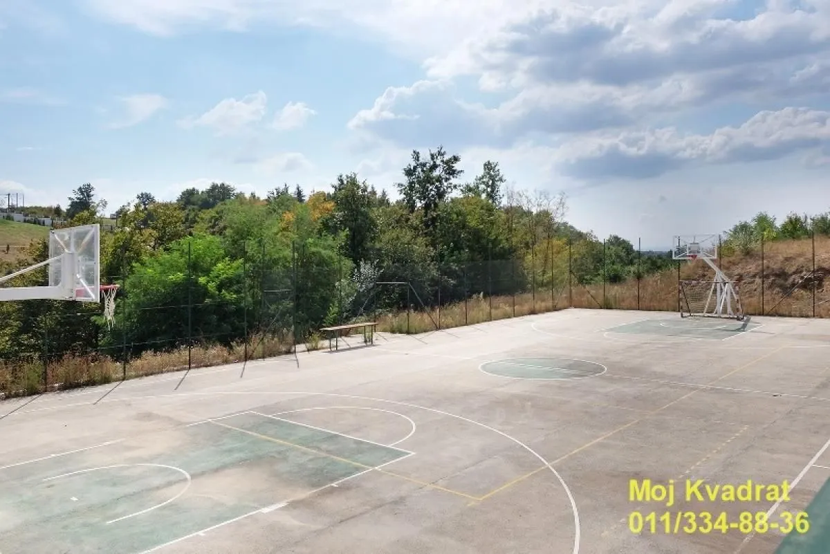 Outdoor sports court with basketball hoops surrounded by greenery.