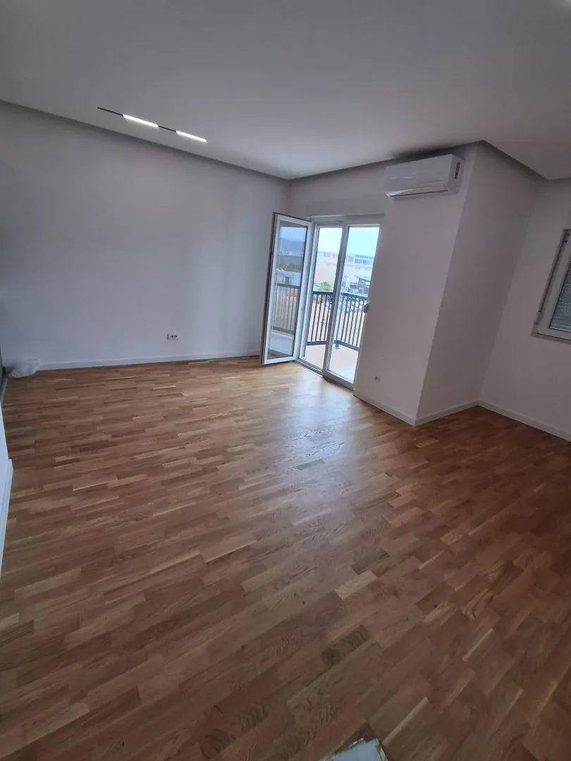 Empty room with wooden flooring, air conditioning unit, and balcony doors.