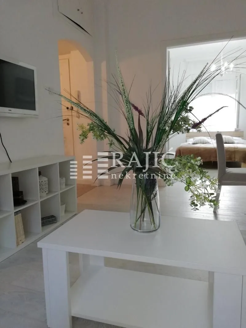 Living room with white furniture, a vase of flowers, and a view into the bedroom.