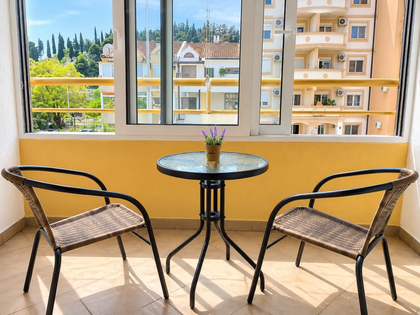 Glazed terrace with a small table, two chairs, and a city view.