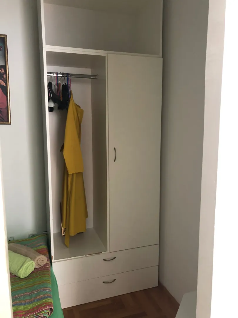 Small white wardrobe with an open section and hangers in the room.