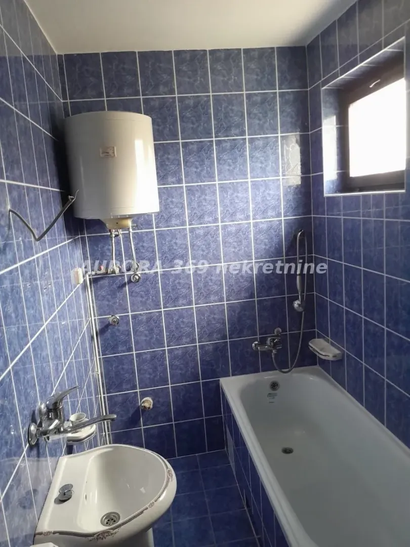 Kupatilo obloženo plavim pločicama sa kadom, umivaonikom i bojlerom.