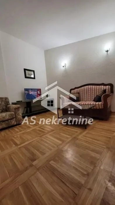 Dnevni boravak sa garniturom, stočićem i televizorom.