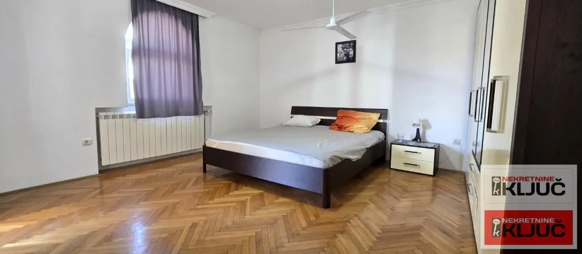 Spacious bedroom with a double bed, parquet flooring, and a large wardrobe.