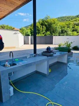 Natkriveni spoljni prostor sa betonskim šankom, sudoperom i pogledom na dvorište. - image 4