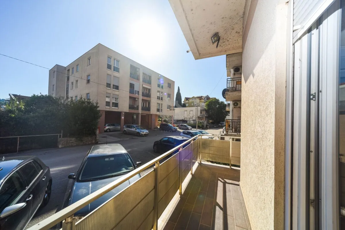 View from the balcony overlooking the street with parked cars and neighbouring buildings.