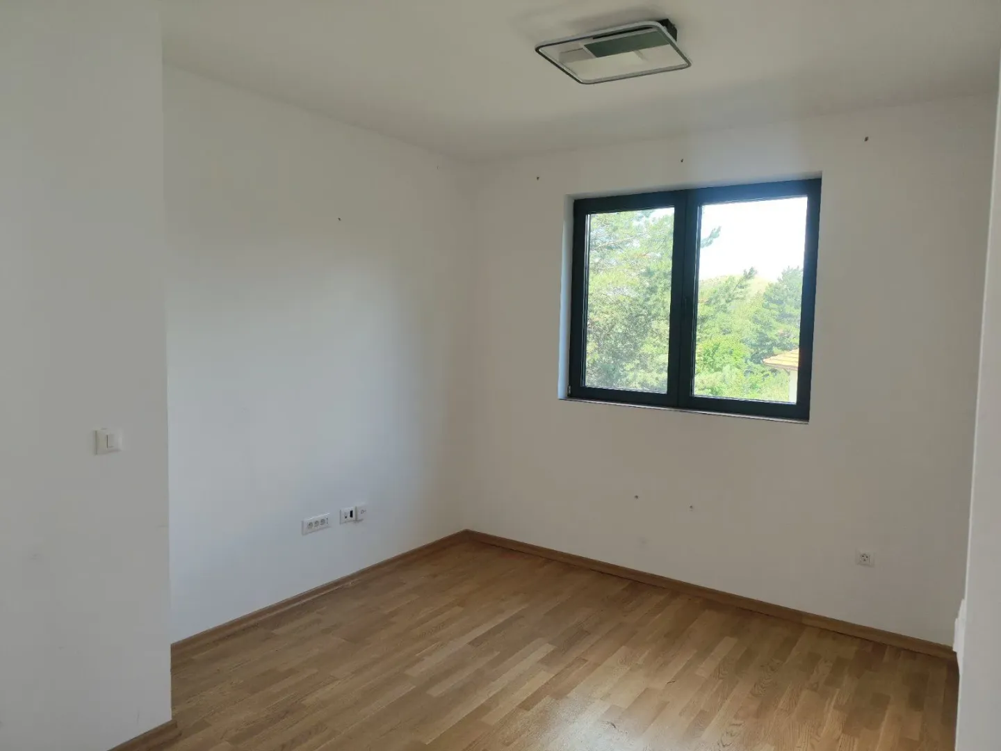 Prazna soba sa parketom i prozorom.