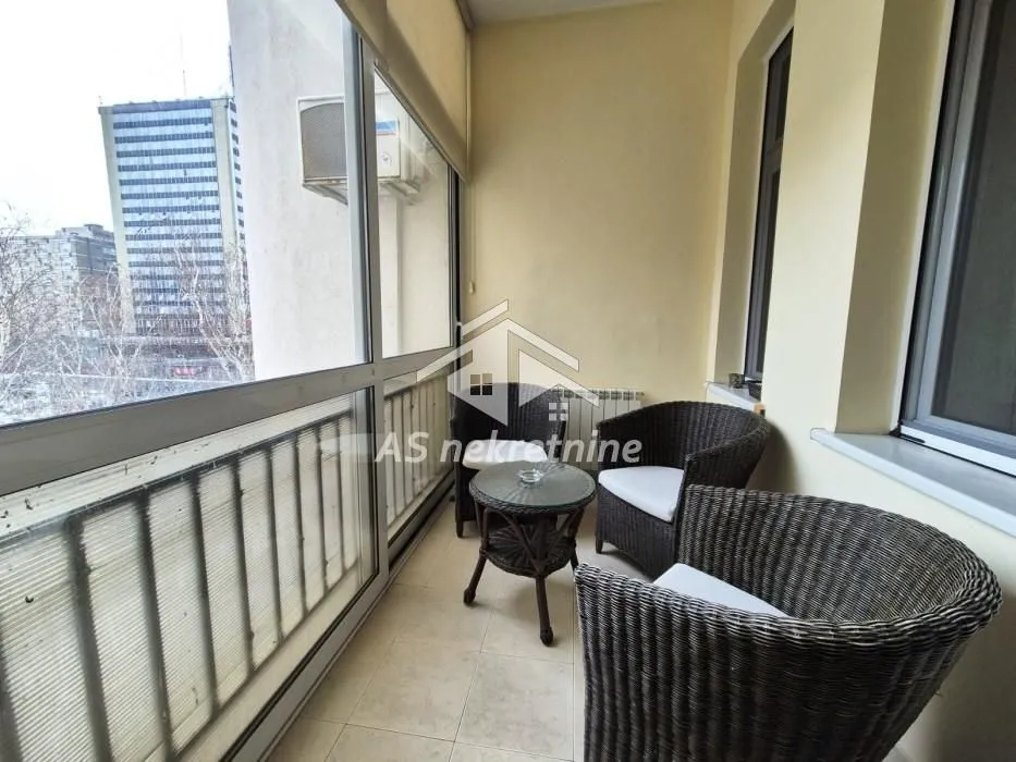 Enclosed balcony with seating furniture and city view.