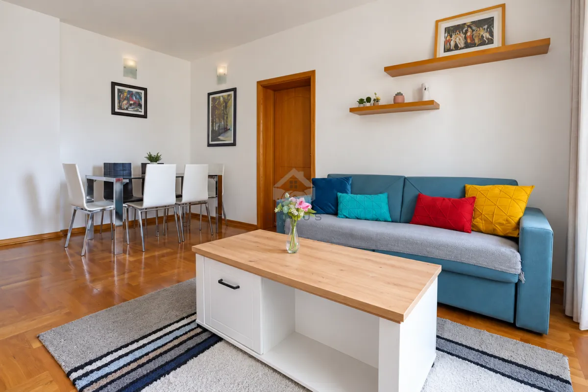 Living room with a sofa, coffee table, and dining area in the background.