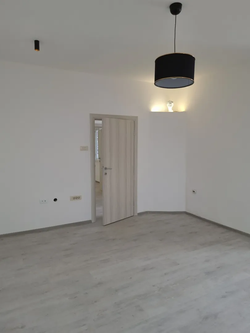 Empty room with light laminate flooring, white walls, and a black pendant light.