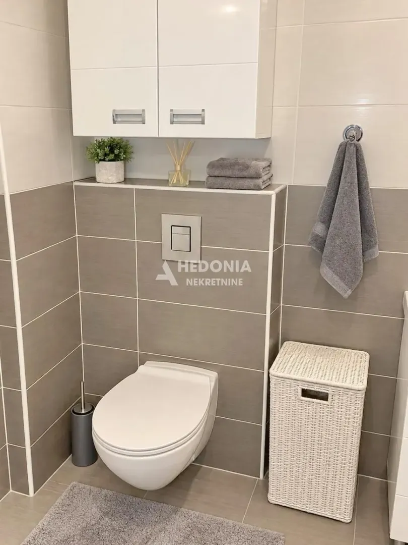 Moderno uređeno kupatilo sa WC šoljom, ormarićem i detaljima u sivim tonovima.