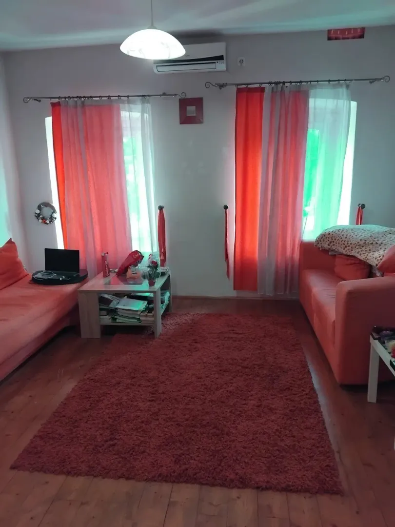 Dnevna soba sa garniturom, stočićem i prozorima sa crvenim zavjesama.