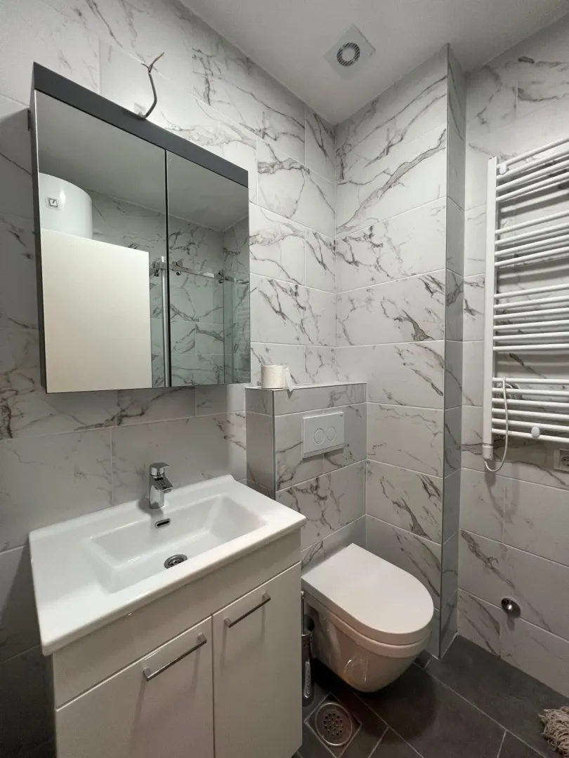 Modernly equipped bathroom with marble tiles, sink, and toilet.