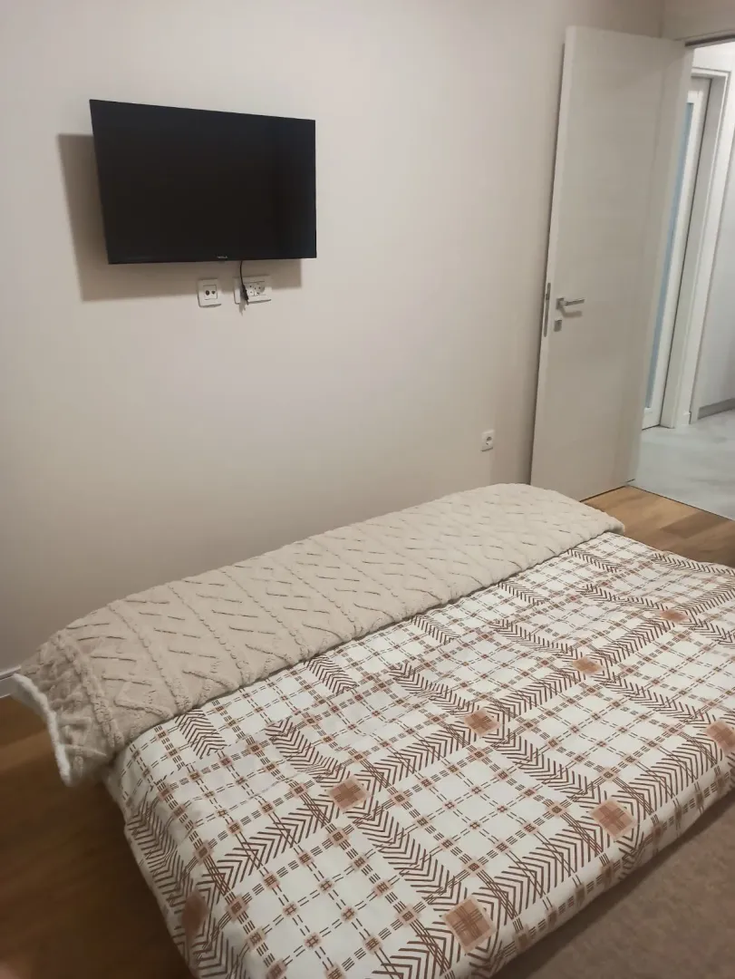Svijetla spavaća soba sa televizorom montiranim na zidu i namještenim krevetom.