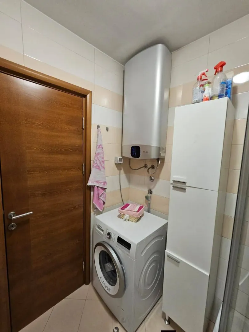 Kupatilo sa veš mašinom, bojlerom i bijelim ormarićem.