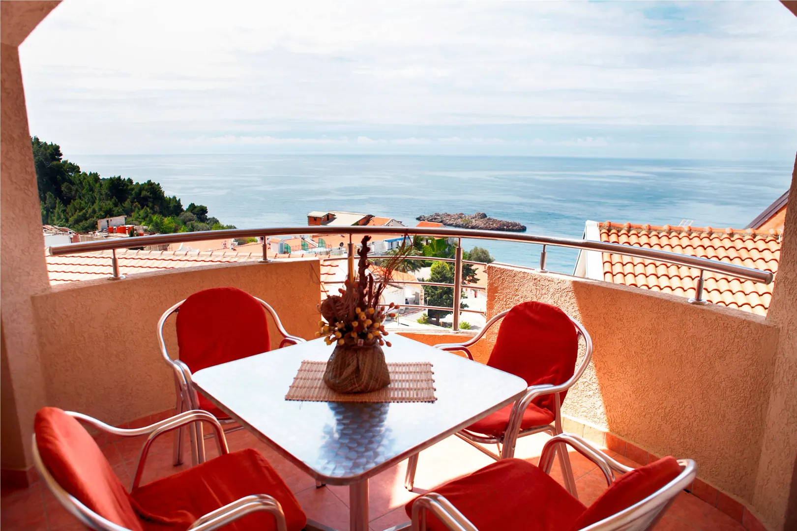 Furnished terrace with a table and four red chairs and a sea view.