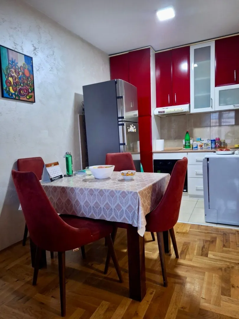 Trpezarijski sto sa stolicama u kuhinji sa crvenim elementima.