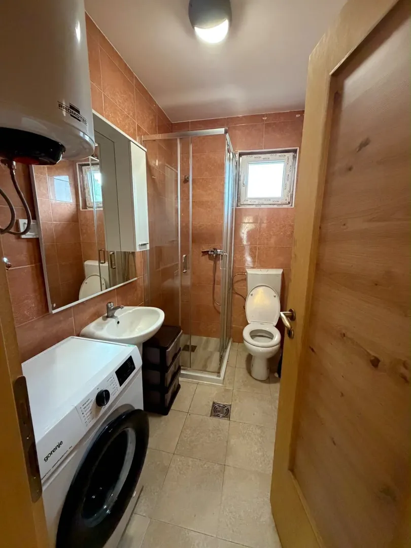 Compact bathroom with a shower cabin, sink, and washing machine.
