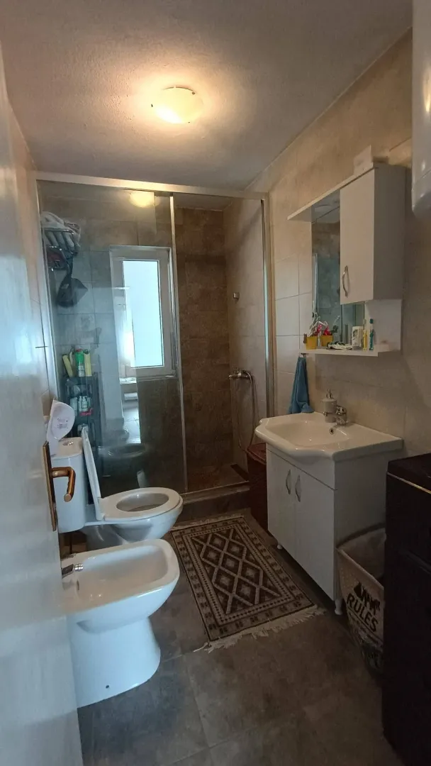 Manje kupatilo sa tuš kabinom, umivaonikom i sanitarijama.