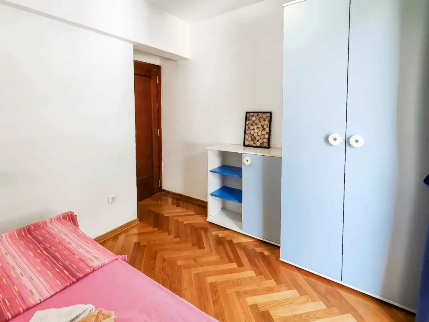 Smaller bedroom with a bed, blue wardrobe, and parquet flooring.