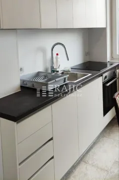 Modern kitchen with white cabinetry, dark countertops, and a built-in oven. - image 3