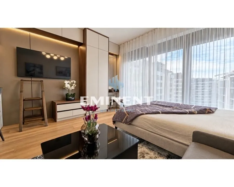 Furnished bedroom with a double bed, TV, and large windows.