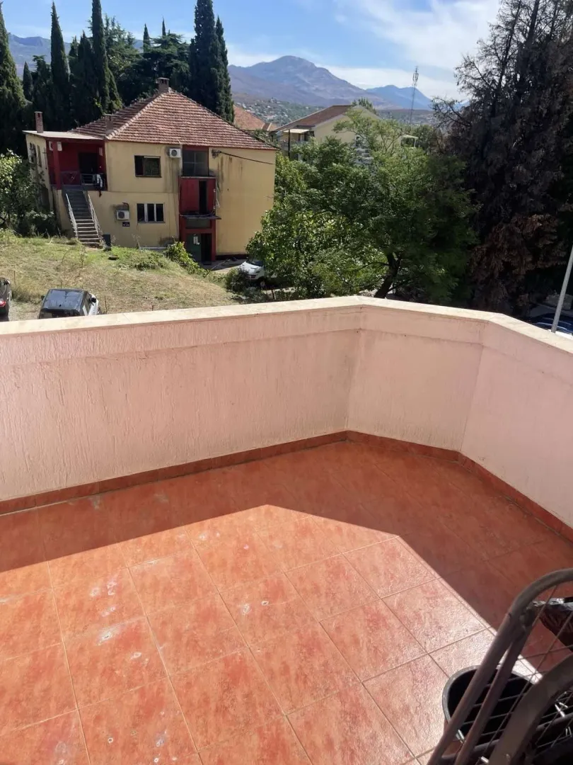 An open terrace tiled with red ceramics, offering a view of the surrounding area and mountains.