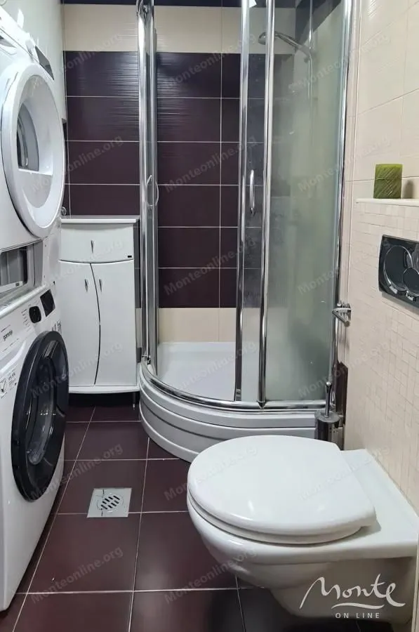 Bathroom with a shower cabin, toilet, and stacked washing and drying machines.