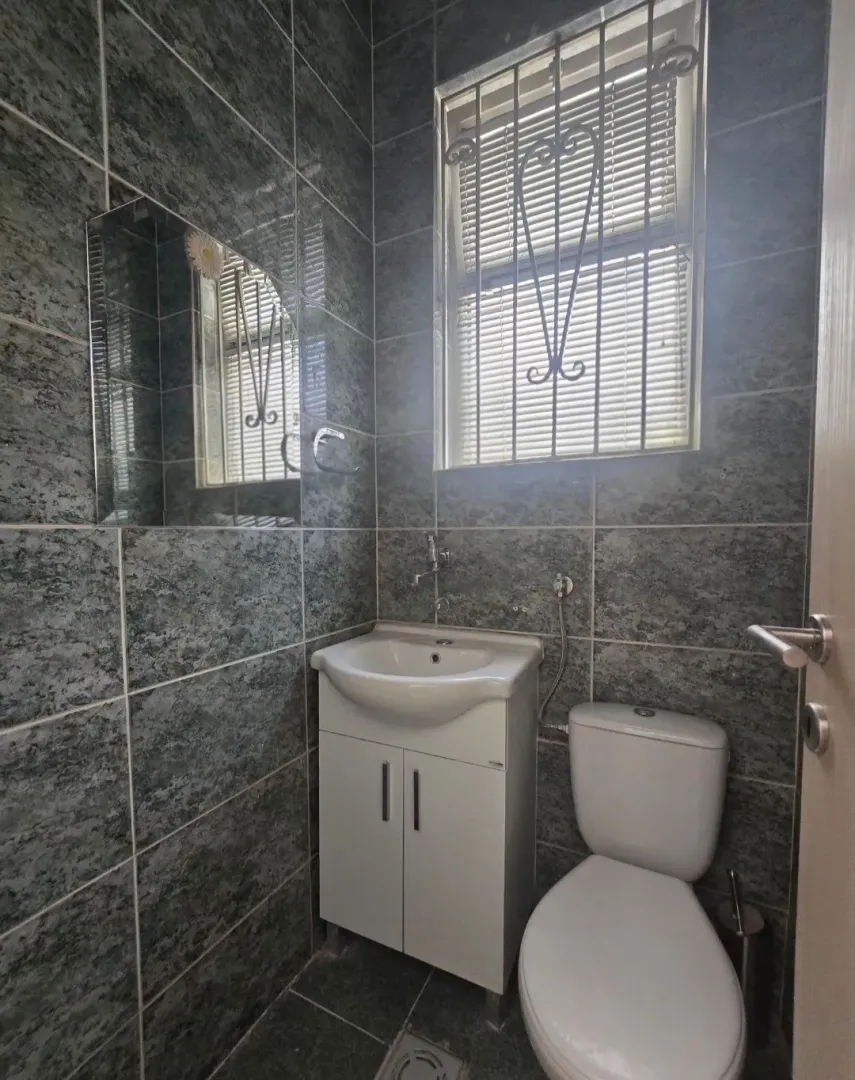 Small bathroom tiled in grey with a sink and toilet.