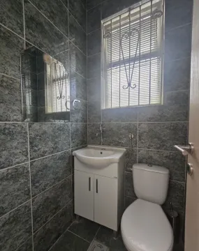 Small bathroom tiled in grey with a sink and toilet. - image 9