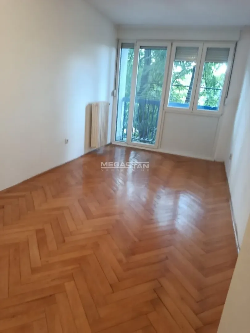 Prazna prostorija sa parketom i izlazom na balkon.