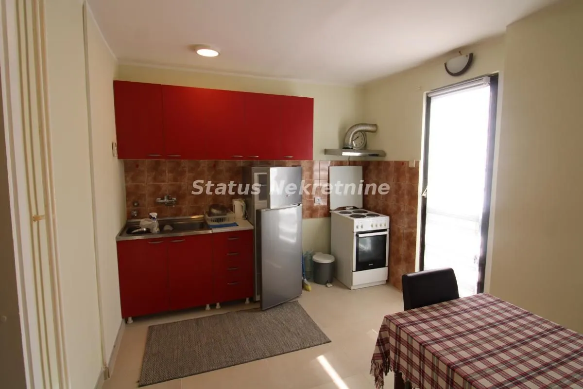 Manja kuhinja sa crvenim elementima i trpezarijskim stolom.