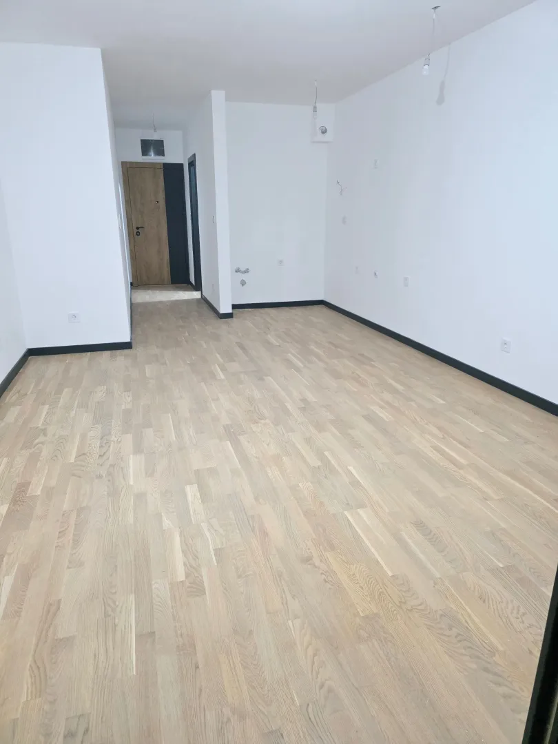 Prazna soba sa svijetlim parketom i bijelim zidovima.