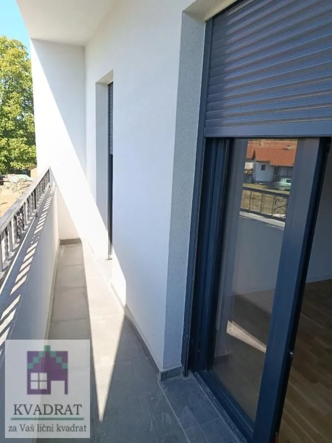 Uski popločani balkon sa staklenim balkonskim vratima i roletnama.