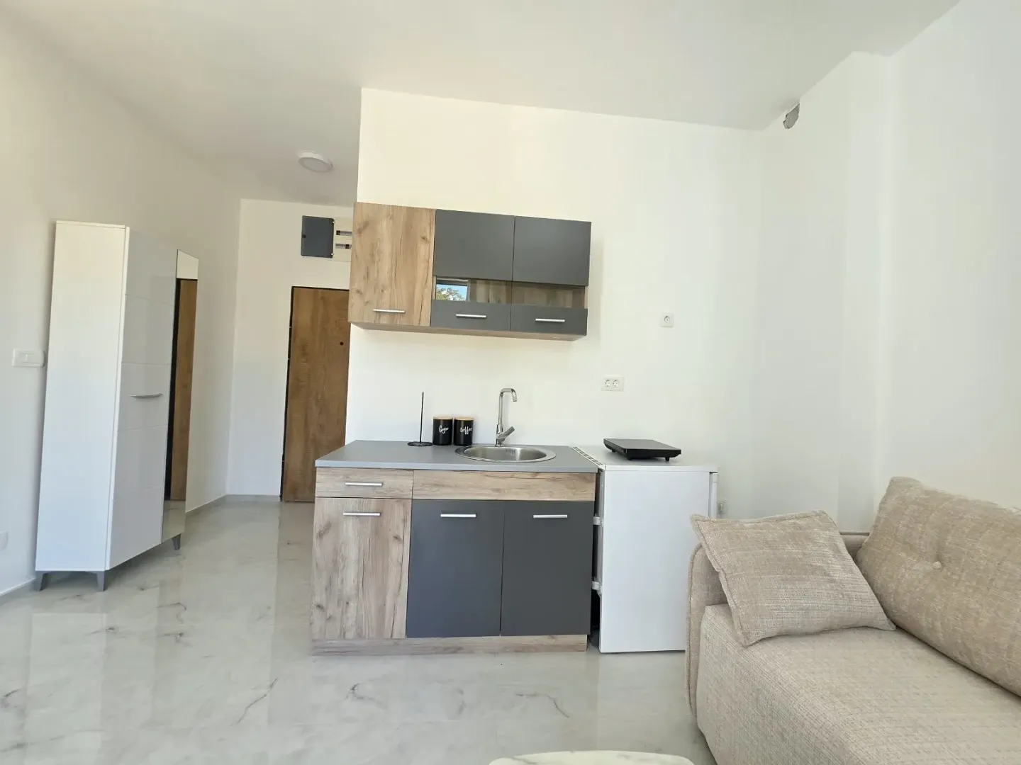 Small kitchen with a sink, wood-and-grey cabinets, and a sofa in the corner.