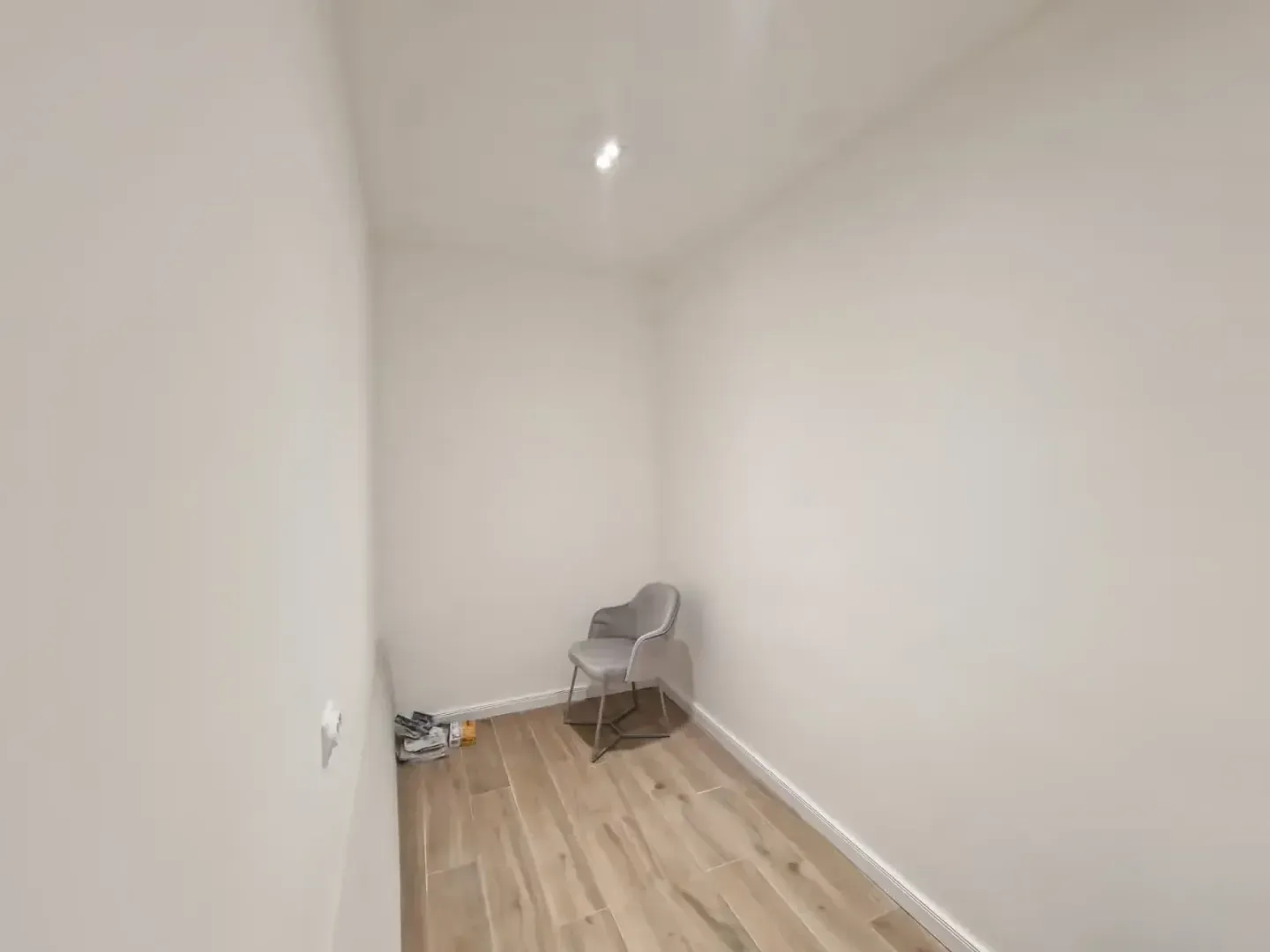 Small empty room with white walls and a grey chair in the corner.
