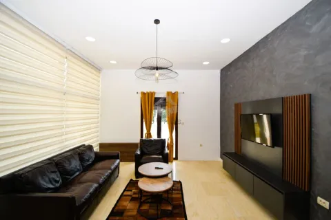 Living room with a leather sofa, TV unit, and a large window with roller blinds. - image 9