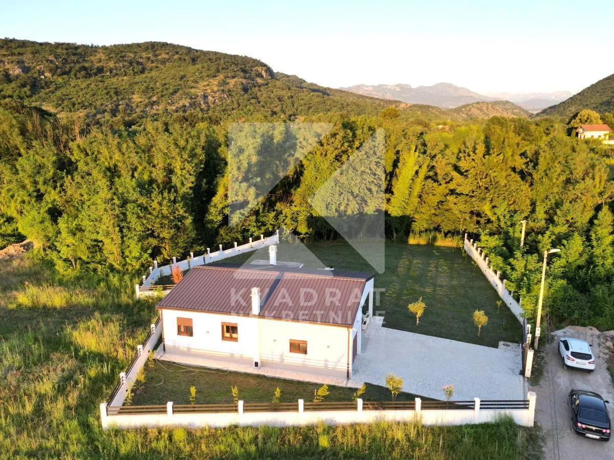 Aerial view of a single-story house with a yard and fence in nature.