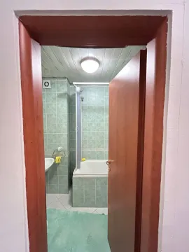 Pogled iz hodnika na kupatilo obloženo zelenim pločicama sa kadom. - image 15