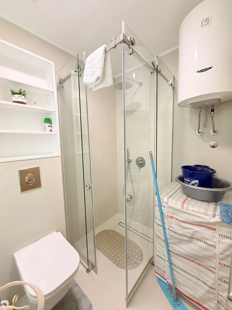 A cluttered bathroom with a glass shower enclosure and a water heater.
