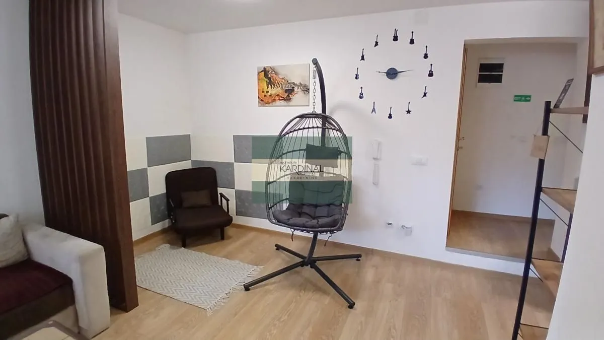 Dnevna soba sa foteljom, visećom stolicom i dekorativnim satom na zidu.