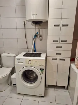 Kupatilo opremljeno WC šoljom, veš mašinom, bojlerom i bijelim ormarićem za odlaganje. - image 7