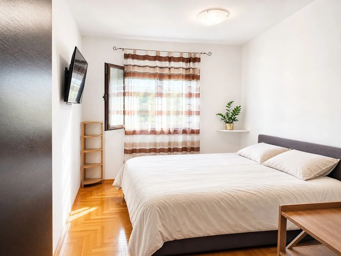 Bedroom with a double bed, a window with curtains, and a wall-mounted TV.