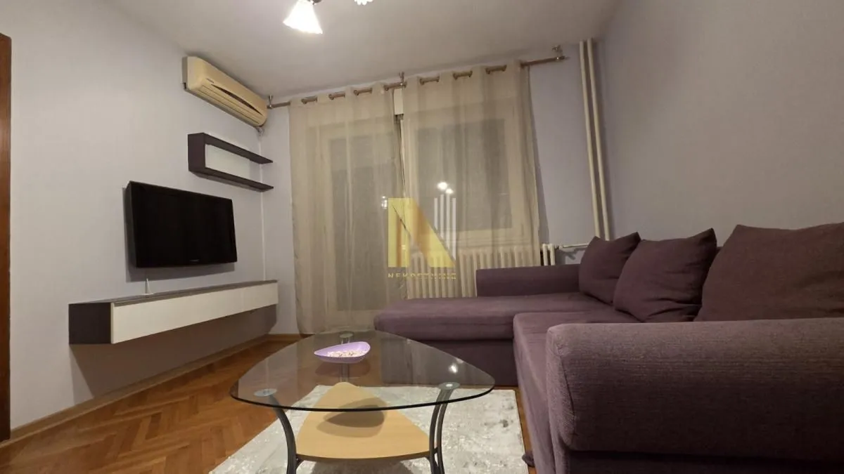 Dnevna soba sa ugaonom garniturom, televizorom i klima uređajem.