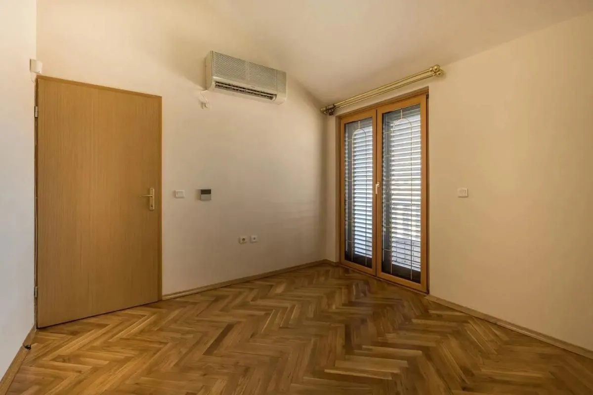 Empty room with wooden parquet flooring, an air conditioning unit, and balcony doors.